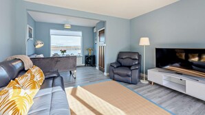 A modern living room with a sofa, a recliner, a TV, and a view of the sea through large windows. - 2 Bed in Amble (oc-l28057) (Amble)