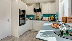 A modern kitchen with white cabinetry, a built-in oven, a stainless steel range hood, and a teal backsplash. - 2 Bed in Amble (oc-l28057) (Amble)
