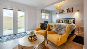 A modern bedroom with a bed, two yellow armchairs, a round table with fruit, and a large window. - 1 Bed in Newquay (oc-l28083) (Newquay)