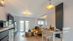 A modern kitchen with a microwave, a dining area with a white table and chairs, and a living area with a sofa and a coffee table. - 1 Bed in Newquay (oc-l28083) (Newquay)