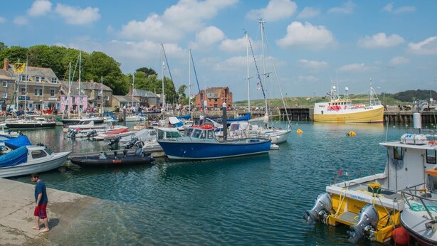 A marina with various boats docked, a person standing on the dock, and buildings in the background. - 2 Bed in Winnards Perch (oc-w28086) (Winnard's Perch)