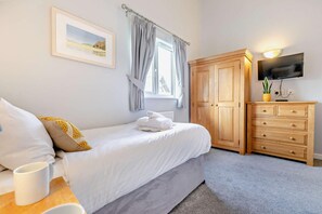 A bedroom with a bed, a wooden dresser, a television, and a window with curtains.