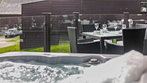 A hot tub with a glass enclosure, outdoor wicker furniture, and a wooden building in the background. - 2 Bed in Winnards Perch (oc-w28086) (Winnard's Perch)