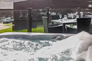 A hot tub with a glass enclosure, outdoor wicker furniture, and a wooden building in the background. - 2 Bed in Winnards Perch (oc-w28086) (Winnard's Perch)