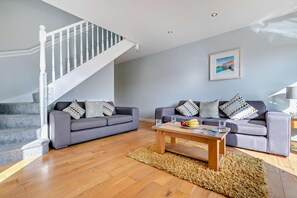 A living room with two grey sofas, a wooden coffee table, and a staircase with white railings.