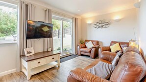 A living room with a TV, leather sofas, a white console table, and a large window. - 2 Bed in Putsborough (oc-a22903) (Croyde)