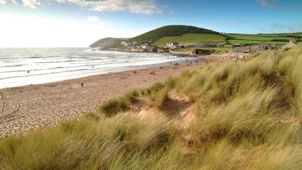 A beach with a grassy foreground, a hill in the background, and buildings along the coastline. - 2 Bed in Putsborough (oc-a22903) (Croyde)