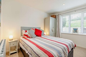 A bedroom with a bed, a nightstand, a wardrobe, and a window with blinds.