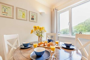 Une table de petit-déjeuner avec des bols et des assiettes bleus, ainsi qu’un vase rempli de tournesols, le tout placé devant un mur blanc orné de tableaux encadrés.