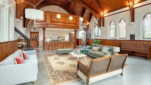 A spacious living area with a high ceiling, wooden beams, a kitchen, and a staircase leading to an upper level. - 3 Bed in Yoxford (oc-t28018) (Aldeburgh)