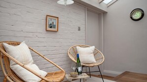 A room with two wicker chairs, a small table with a bottle and glass, and a framed picture on the wall. - 3 Bed in Yoxford (oc-t28018) (Aldeburgh)
