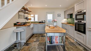 A modern kitchen with a central island, built-in appliances, and a staircase leading to an upper level. - 3 Bed in Lynton (oc-n28090) (Lynmouth)
