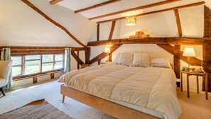 Une chambre avec un grand lit, des poutres en bois, une fenêtre et une table de chevet avec une lampe.