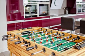 A foosball table in a room with a modern kitchen in the background. - 5 Bed in Tavistock (oc-m28107) (Tavistock)