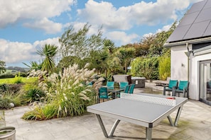 An outdoor patio with a ping pong table, green chairs, and a barbecue area.