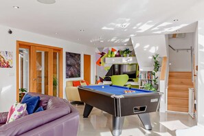 A modern living room with a pool table, a sofa, and a staircase leading to an upper level.