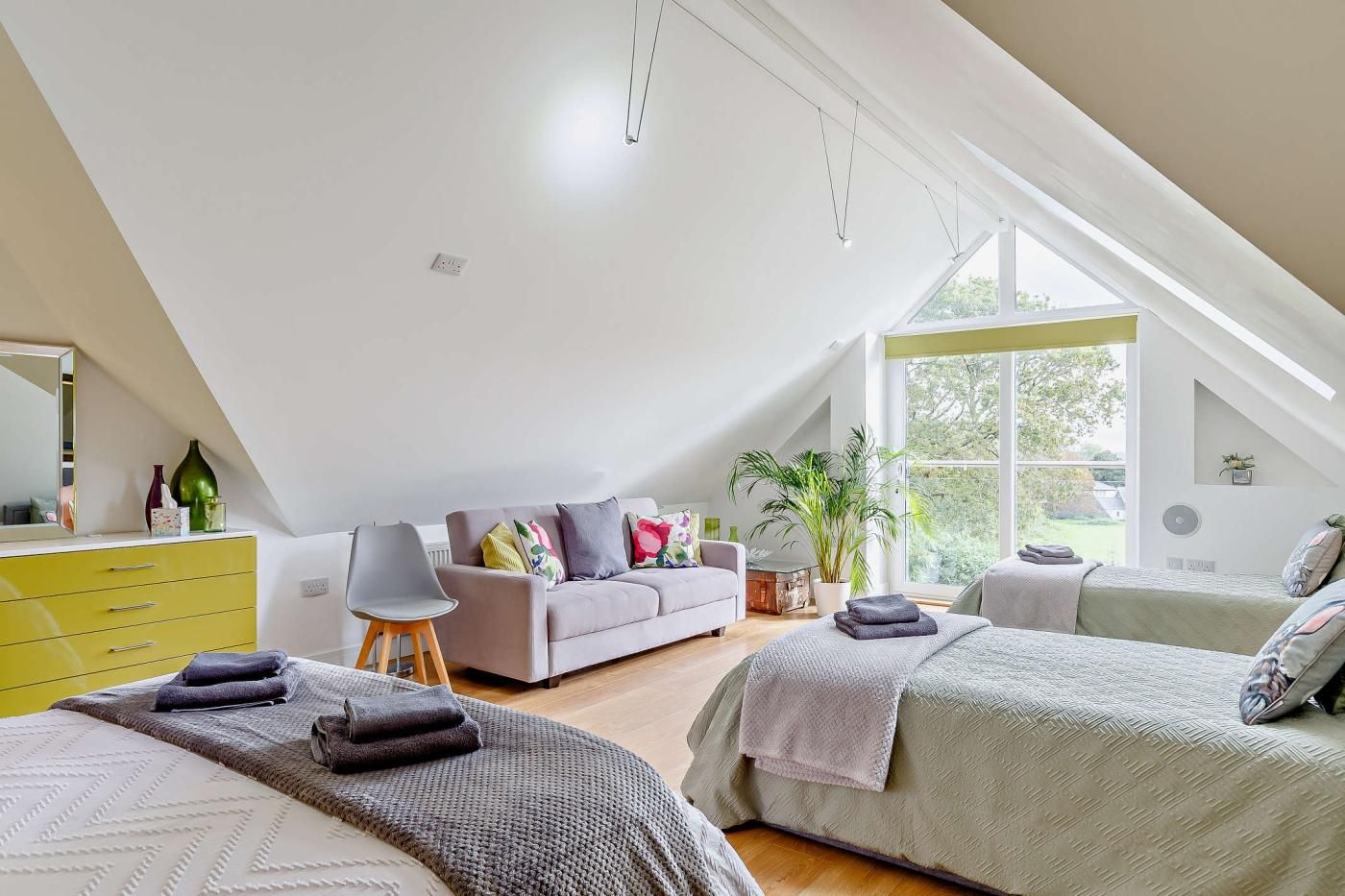 Un dormitorio moderno con techo inclinado, un sofá, dos camas, una silla y un ventanal grande.