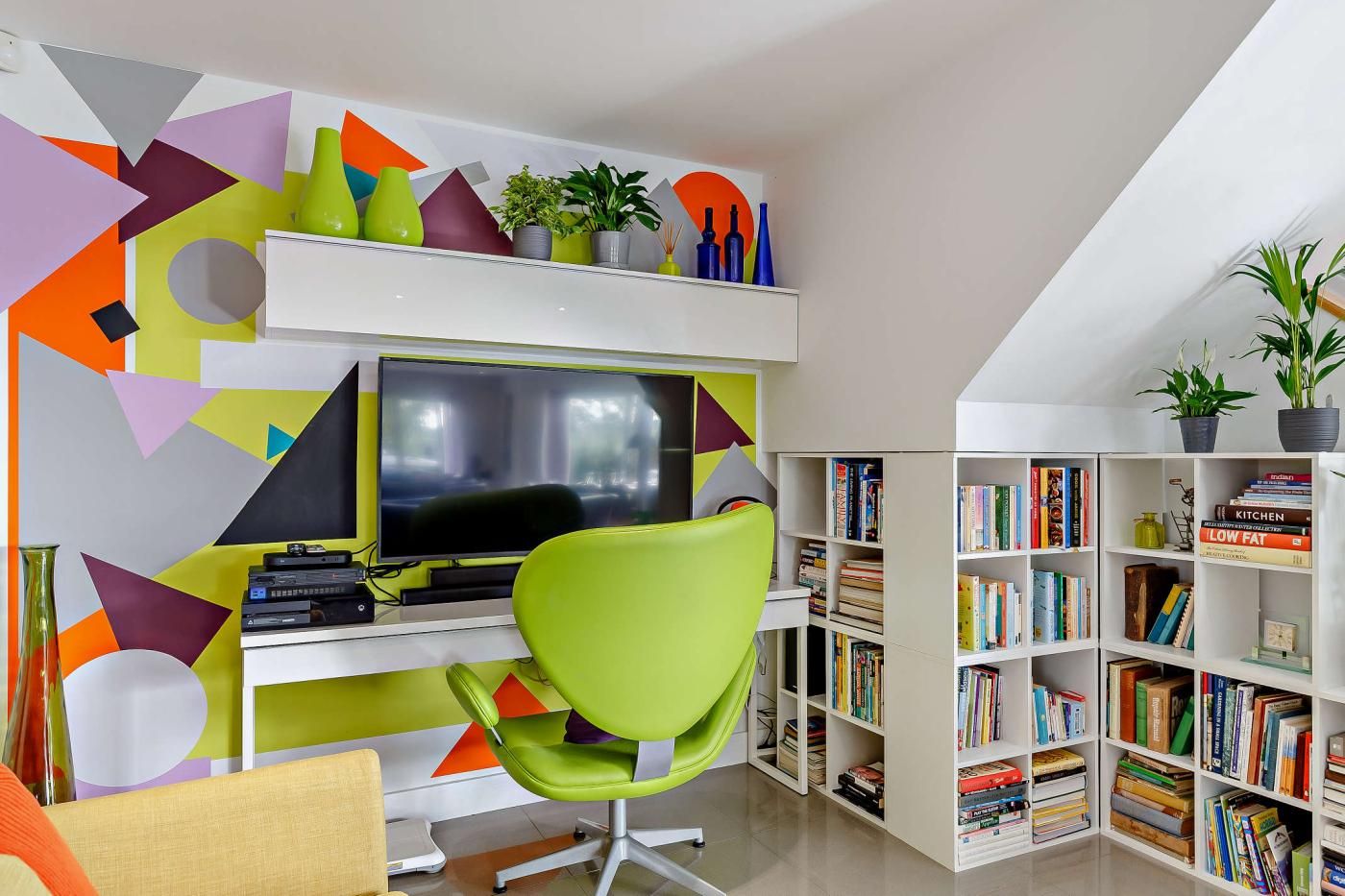 Un moderno ufficio domestico con scrivania, computer e sedia verde. Librerie piene di libri e oggetti decorativi.
