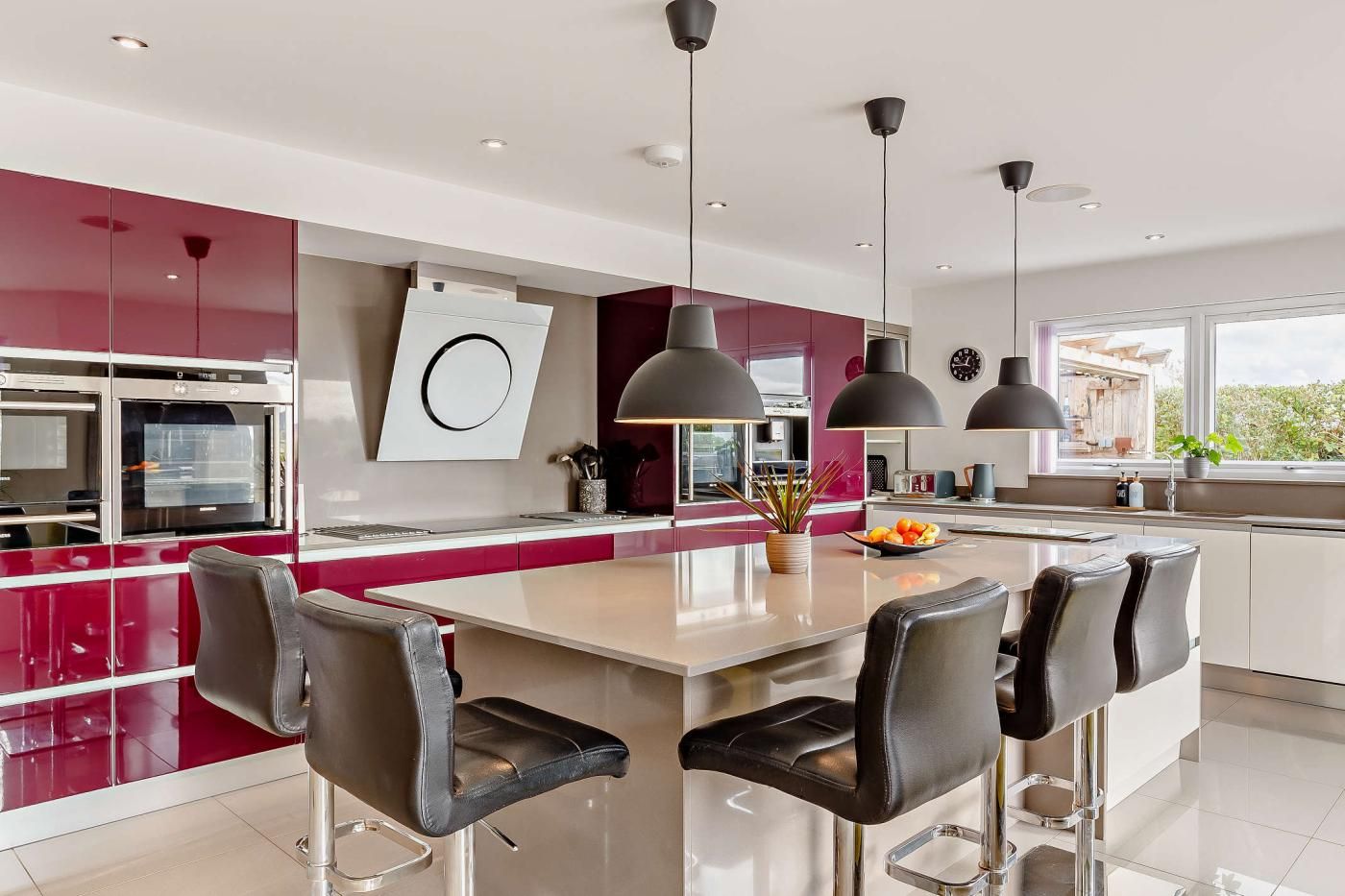 Une cuisine moderne dotée d’un îlot central, de luminaires suspendus et offrant une vue sur l’extérieur.