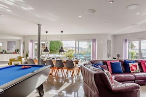 A modern living room with a pool table, a leather sofa, and a dining area with natural light. - 5 Bed in Tavistock (oc-m28107) (Tavistock)
