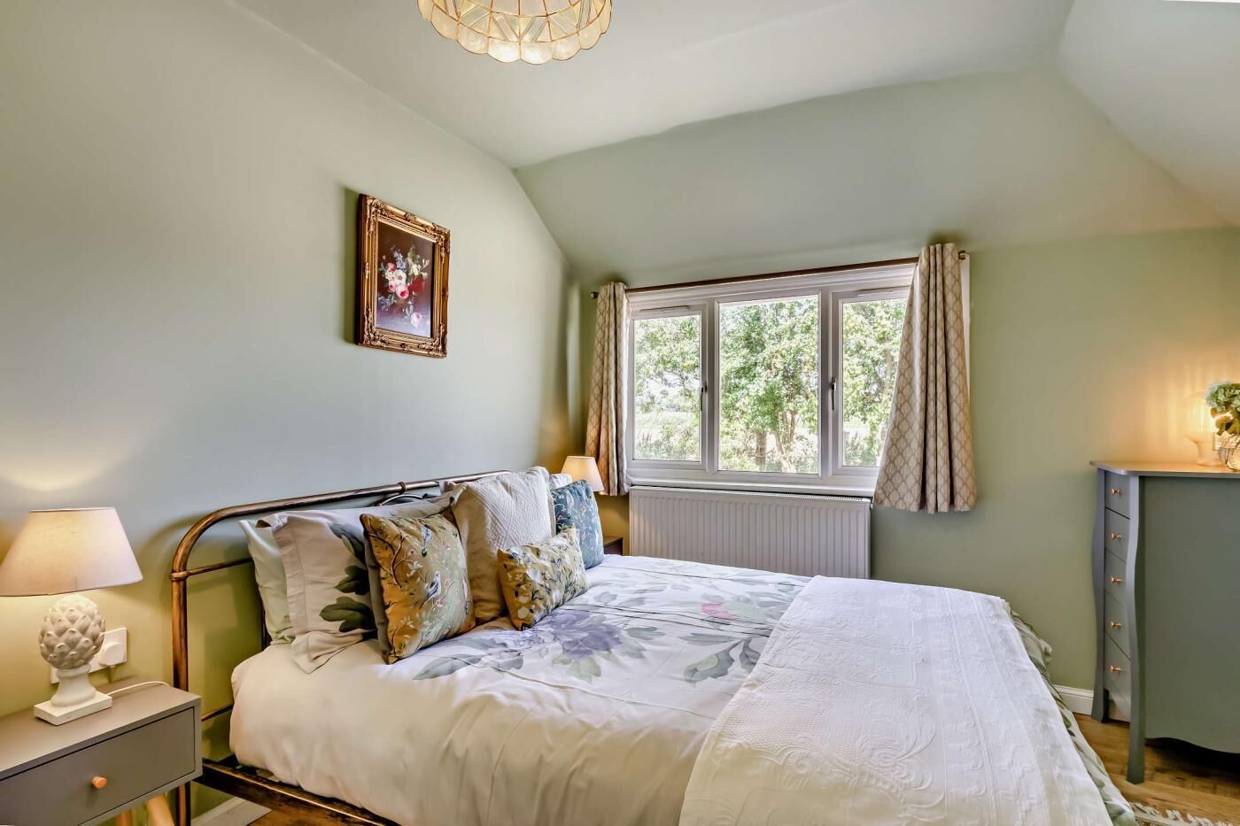 Un dormitorio con cama, mesita de noche, lámpara y ventana con cortinas.