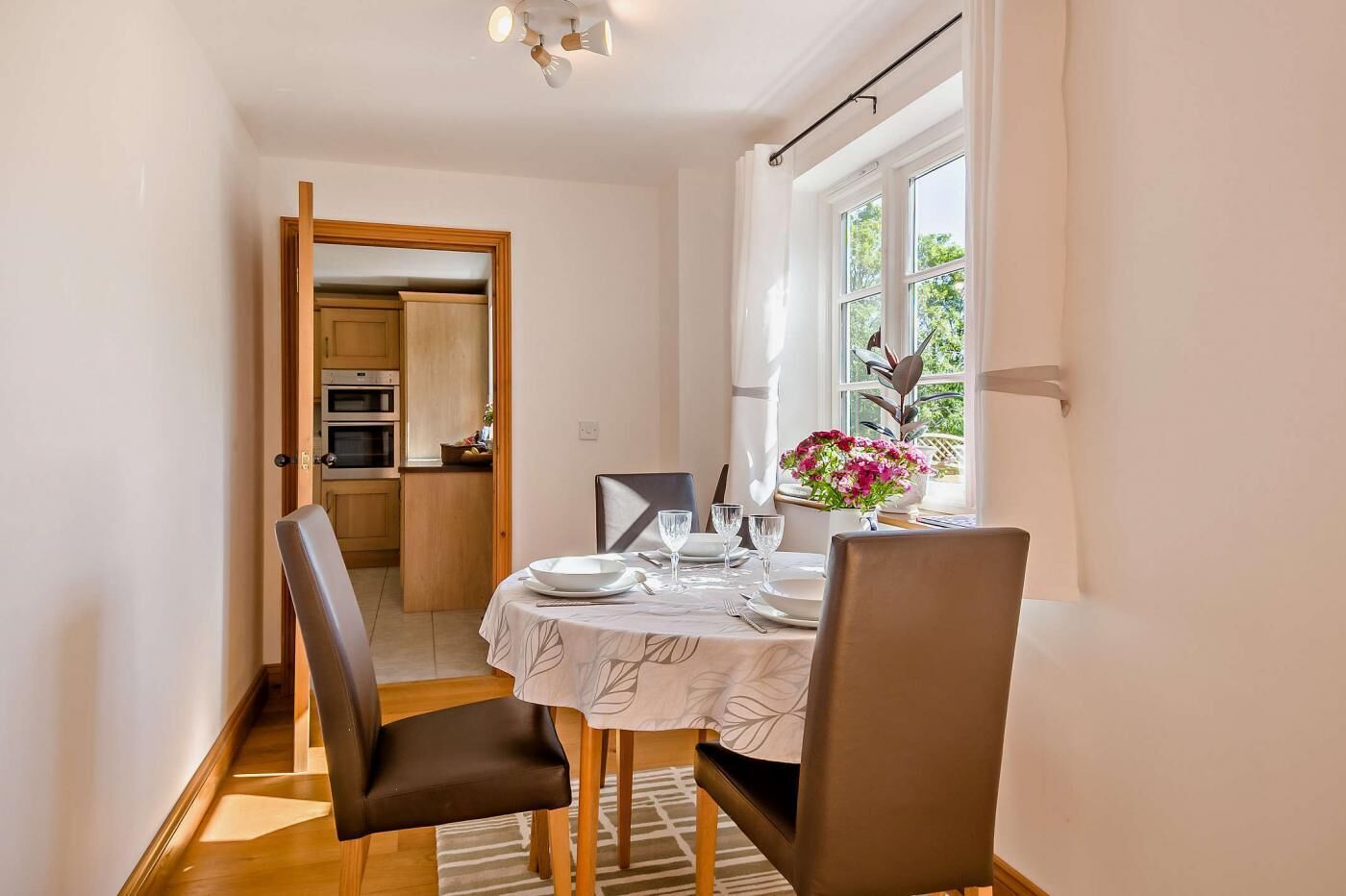 A dining area with a table set for four, a window with curtains, and a view of the outdoors.