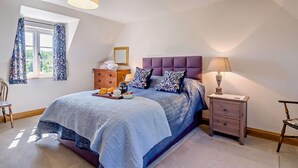 Une chambre à coucher avec un grand lit, une commode, une table de chevet, une chaise et une fenêtre avec des rideaux.