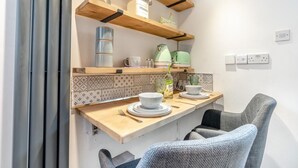 Una cocina con estantes de madera, una tetera, una tetera verde, una botella y una silla.