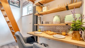 Una cocina compacta con estantes de madera, una tetera, un tostador de estilo vintage y una planta.