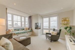 A spacious living room with a large window overlooking the sea, a comfortable seating area, and a motivational quote on the wall. - 2 Bed in Whitstable (oc-b28125) (Whitstable)