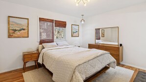 Ein Schlafzimmer mit einem Bett, Nachttischen, einer Kommode, einem Spiegel und Kunstwerken an den Wänden.