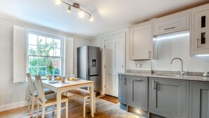 A modern kitchen with a built-in refrigerator, grey cabinets, and a wooden dining table with chairs. - 3 Bed in Whitstable (oc-o28123) (Whitstable)