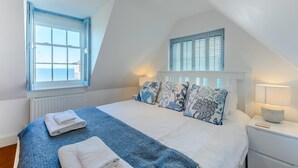 A bedroom with a large bed, a window with shutters, a bedside lamp, and a view of the sea. - 3 Bed in Whitstable (oc-o28123) (Whitstable)