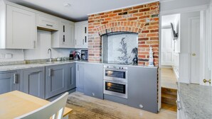 A modern kitchen with grey cabinets, a brick fireplace, and a built-in oven. - 3 Bed in Whitstable (oc-o28123) (Whitstable)