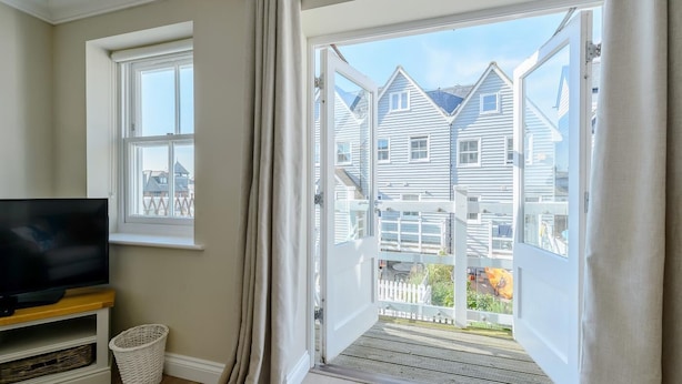 A room with a television on a wooden stand, a wicker basket, and a large window with curtains.