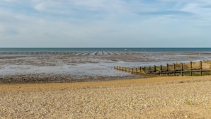 A coastal landscape with a pebbly beach, wooden sea defense structures, and wind turbines in the distance.