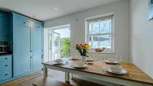 Un coin repas avec une table en bois dressée pour quatre personnes, un meuble de cuisine bleu et une fenêtre donnant sur l’extérieur.