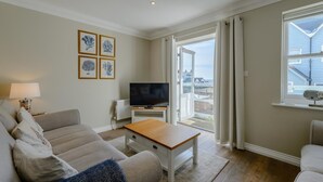 Un salon comprenant un canapé, une table basse, un téléviseur et un balcon avec vue sur la mer.