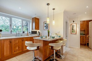 Een moderne keuken met houten kasten, een groot raam, een centraal kookeiland met barkrukken en hanglampen.