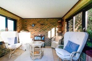 A sunlit room with brick walls, wicker furniture, and a bookshelf.