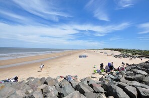 Een strand met een rotsachtige voorgrond, mensen ontspannen en een heldere lucht.