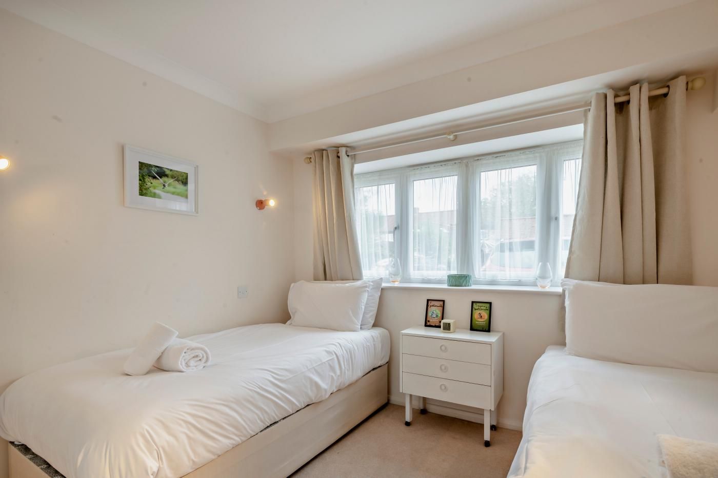 A bedroom with two single beds, a bedside table with a lamp, and a window with curtains.