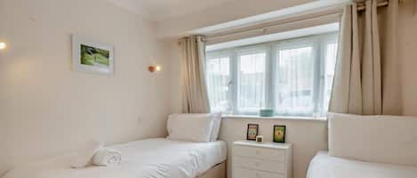 Un dormitorio con dos camas individuales, una mesita de noche con lámpara y una ventana con cortinas.