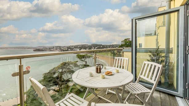 En balkon med bord og stole med udsigt over kysten.