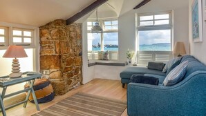 Ett mysigt rum med en vägg av sten, en blå soffa, en lampa och utsikt över havet.
