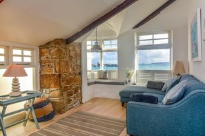 A cozy room with a stone wall, a blue sofa, a lamp, and a view of the sea. - 2 Bed in St. Ives (oc-l28118) (St Ives)