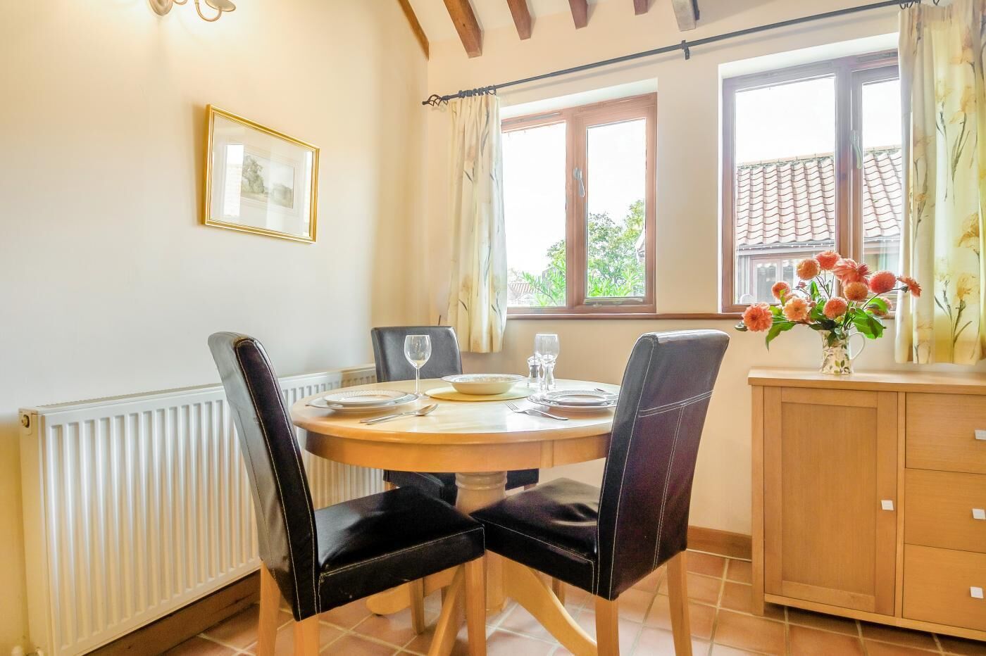Un coin repas avec une table ronde, des chaises noires, un meuble en bois et une fenêtre avec des rideaux.