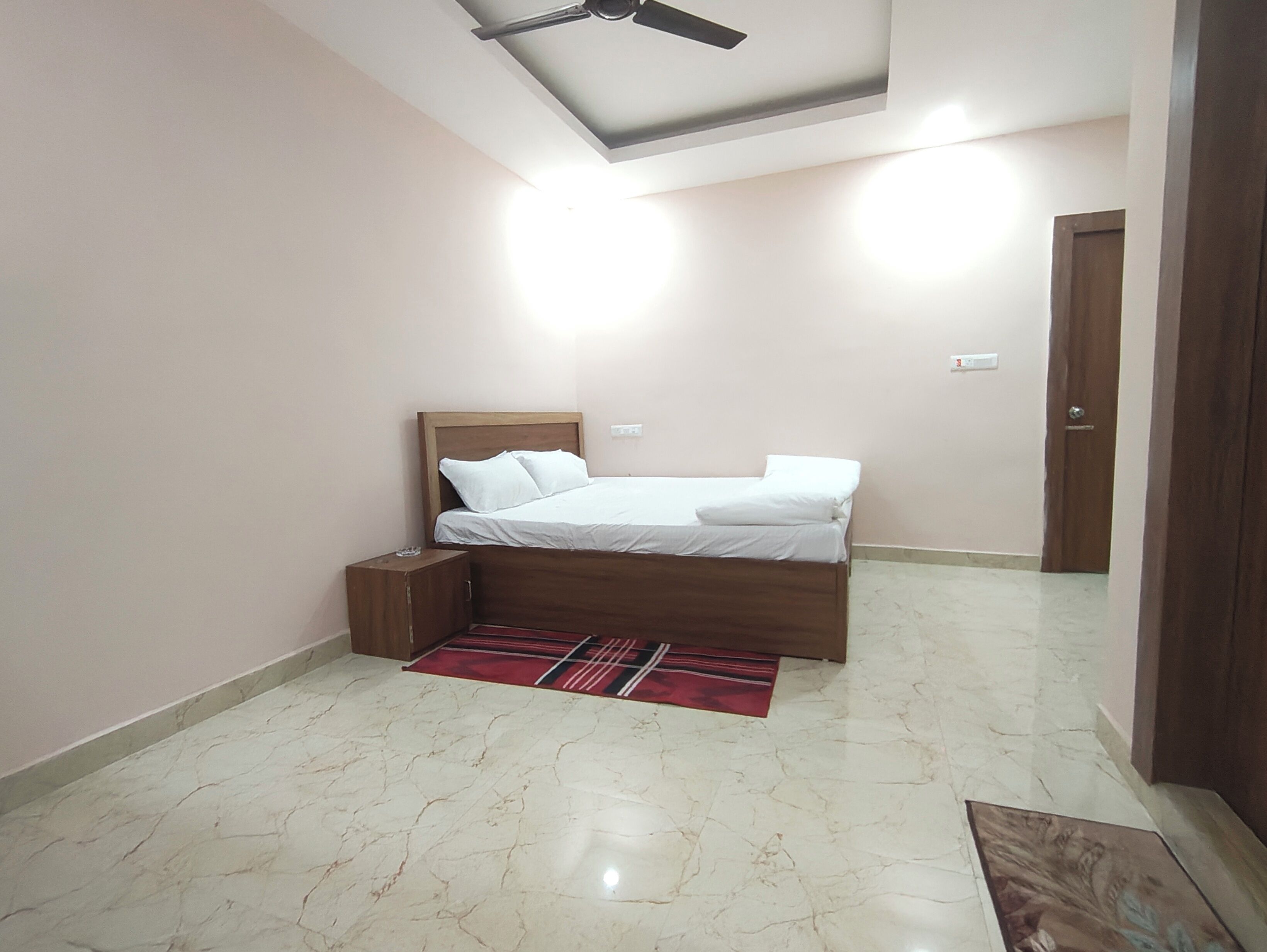 A bedroom with a bed, a nightstand, a ceiling fan, a door, and a marble floor.