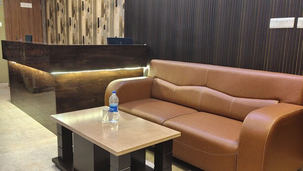 A reception area with a wooden reception desk, a brown leather sofa, and a small table with a water bottle. - HOTEL ARDENT (Ranchi)