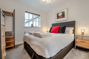 A modern bedroom with a large bed, a window, a headboard, a bedside table, and a shelf unit. - 3 Bed in Padstow (oc-c28137) (Padstow)
